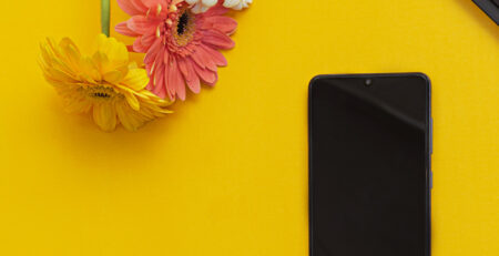 Celular sobre fondo amarillo con teclado a un costado y flores de colores. Negocio creativo, blog de vibra creativa un sitio web de Cely Cruz