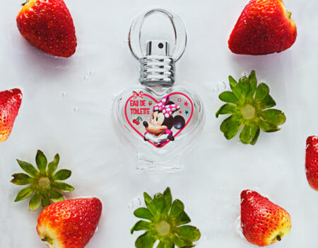 Perfume infantil de Minnie mouse sobre fondo blanco rodeado de fresas rojas todo sobre agua y burbujas. Cely Cruz, Vibra Creativa.