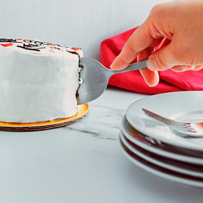 Pastel de San valentín mano cortandolo y en los bordes platos y tenenor. Flat lay para Vibra Creativa. Nathys Sweet colaboración.